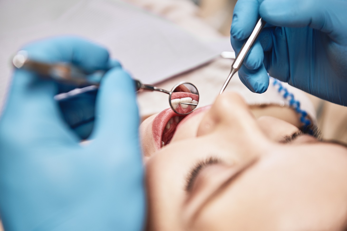 Close-up of woman opening her mouth wide during inspection of oral cavity. Dentist is checking up her teeth using dental tools. Medicine and health care concept. Focus on dental tools. Horizontal shot